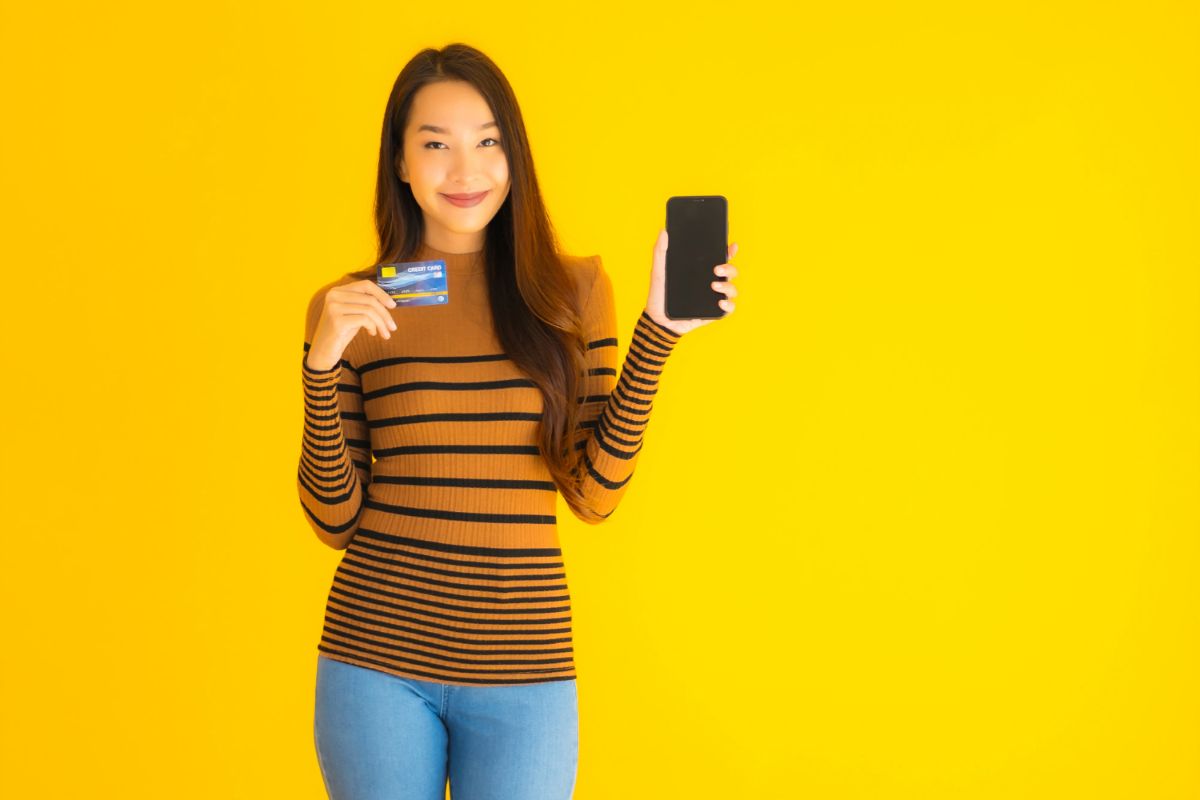 Mulher segura celular e cartão de crédito, representando pagamento por aproximação.