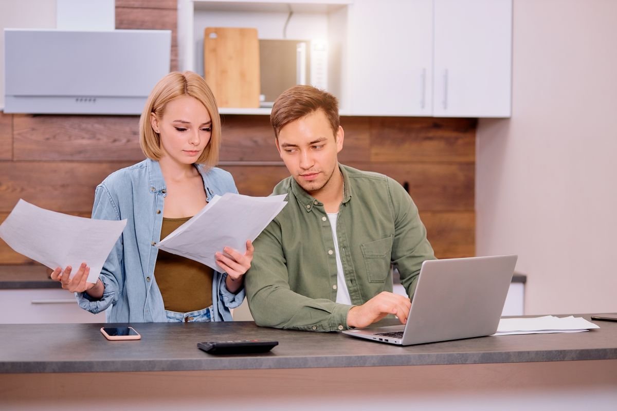 Dos personas en la mesada de una cocina con papeles y una laptop