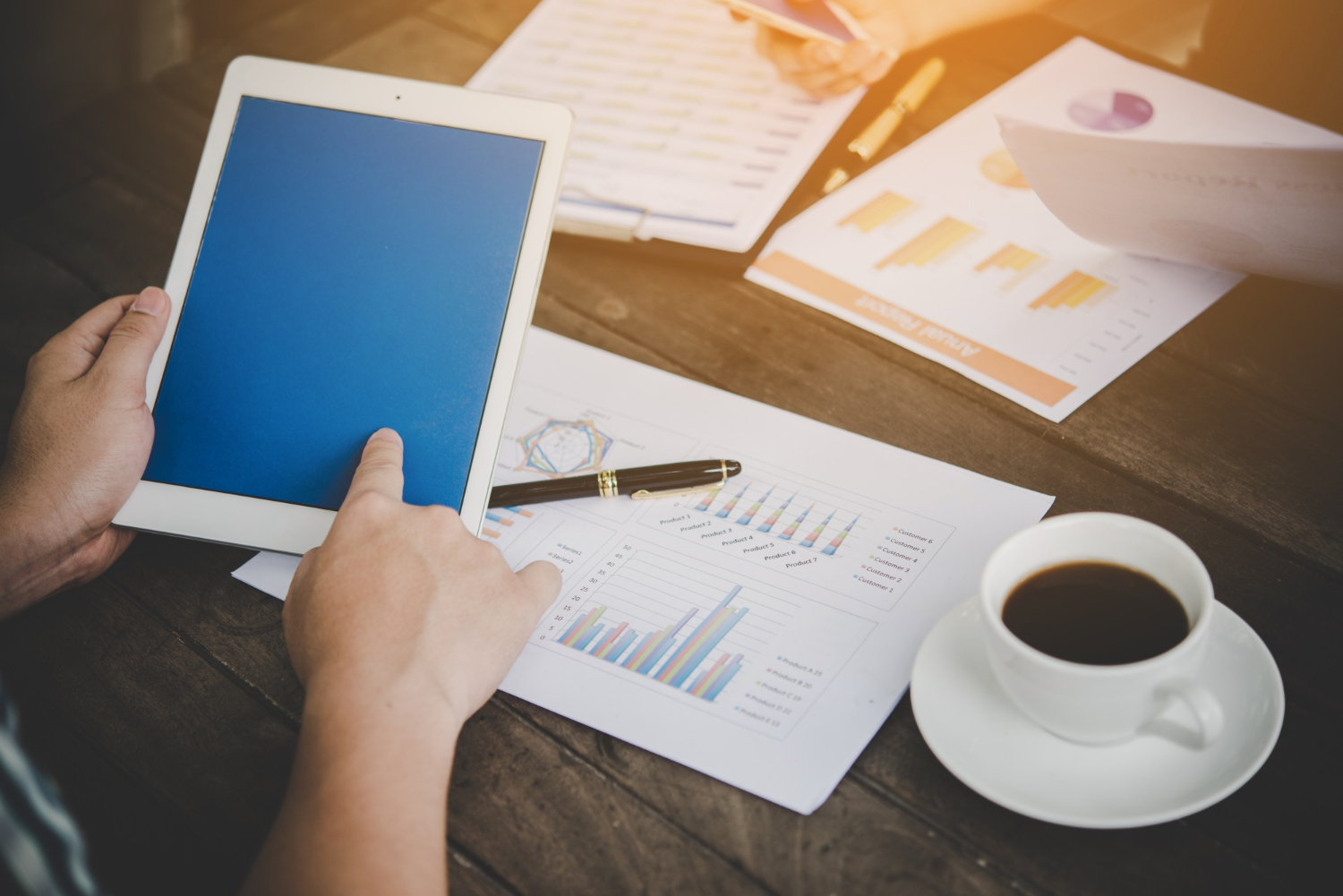 Pessoa analisando gráficos financeiros com tablet sobre mesa