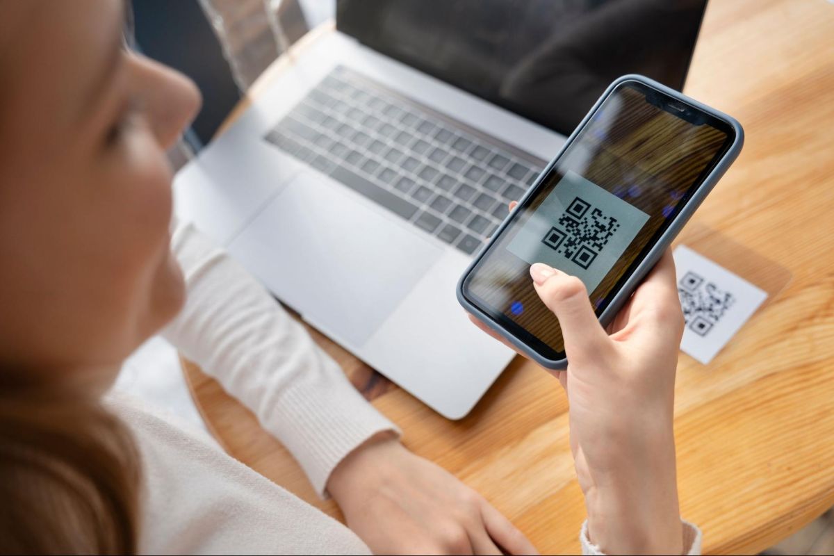 Pessoa escaneando um código QR com o celular, enquanto está ao lado de um laptop