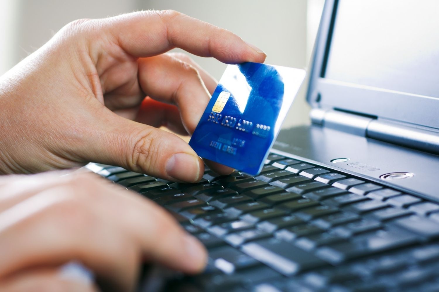 Pessoa segurando cartão de crédito sobre notebook para fazer compra segura.