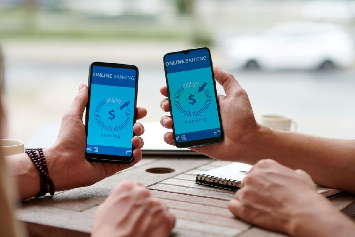 Pessoa segurando iPhone próximo a cartão de crédito realizando pagamento por aproximação.