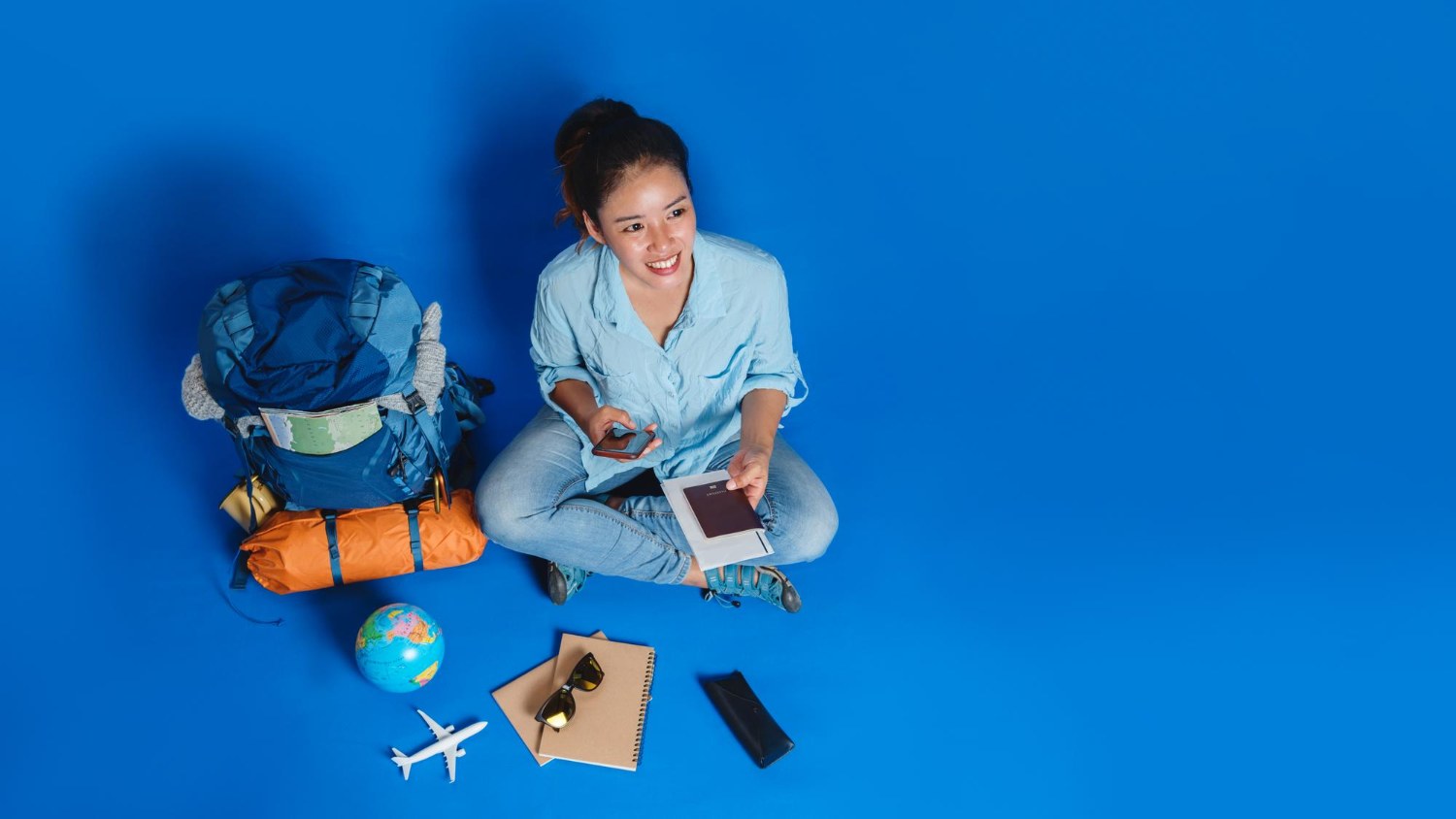 Mulher com mala, celular e documentos planejando sua viagem