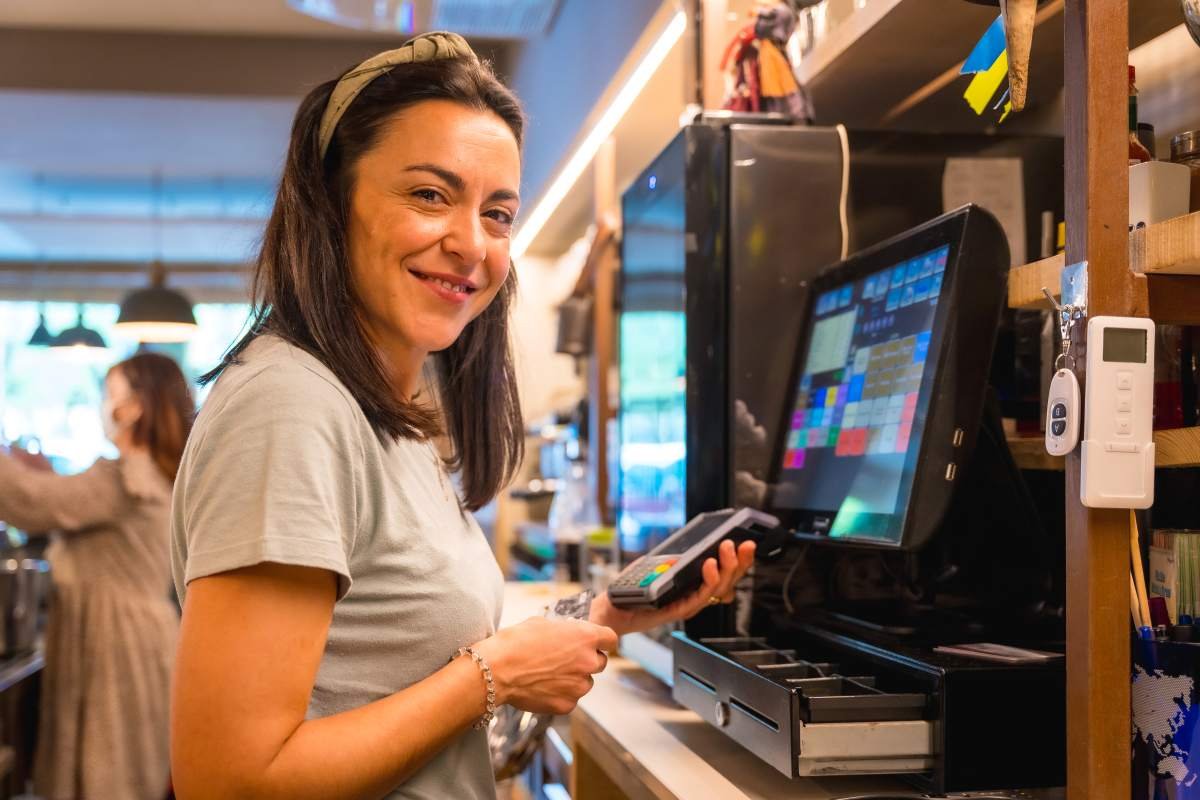 Empreendedora analisando relatório de vendas na tela da maquininha Point Pro 3 em balcão de loja.