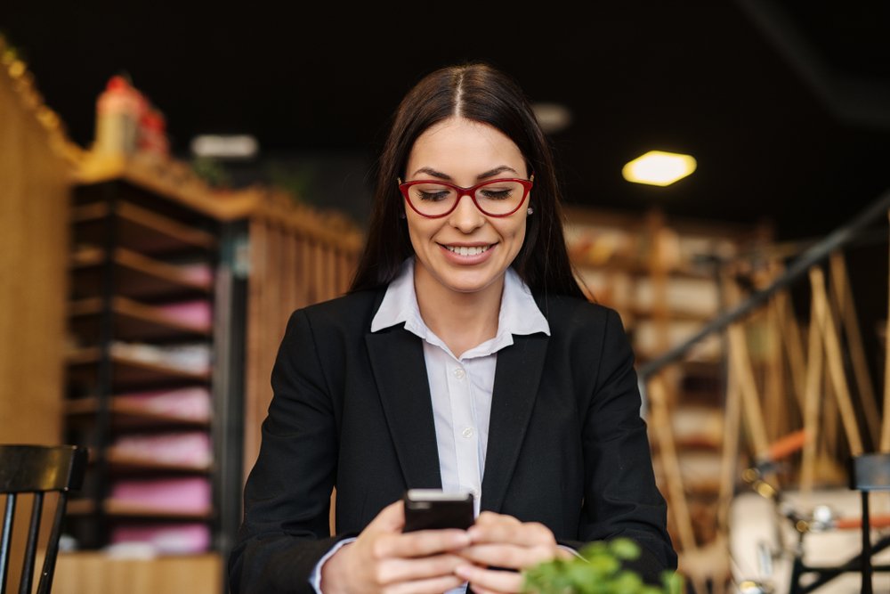 Empreendedora consultando o celular durante a gestão de pedidos e documentos do negócio.